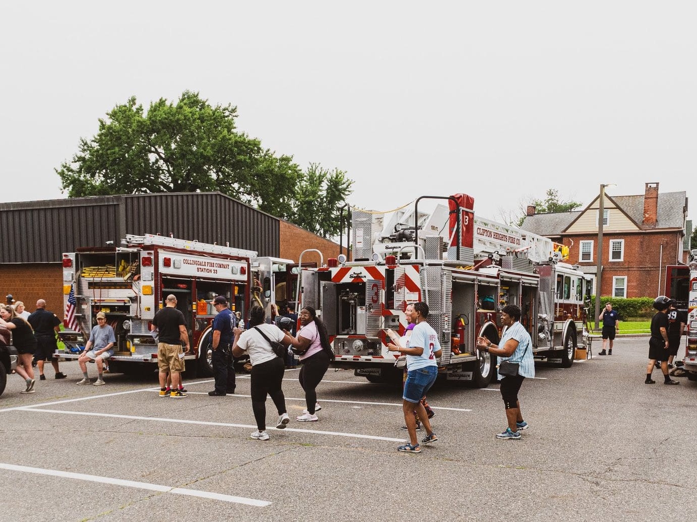 People dancing in a parking lot during a community event, with firetrucks parked in the background.
