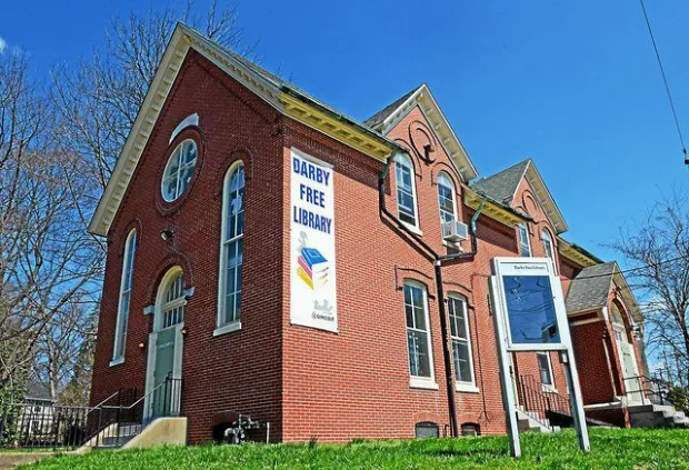Exterior view of the historic Darby Library in Darby, PA showing its brick facade, front steps, and surrounding greenery.