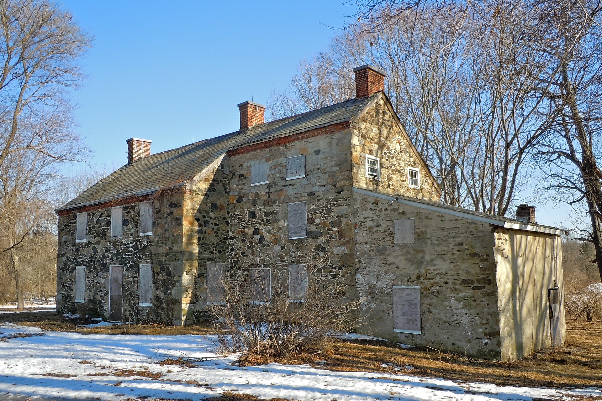 A historic white farmhouse with a pitched roof and central chimney surrounded by open grassy fields. A weathered wooden fence runs in front of the property, and large trees stand in the background under a partly cloudy sky. The scene depicts the Squire Cheyney Farm in Thornbury Township, Pennsylvania, illustrating the rural agricultural character of the area’s past.