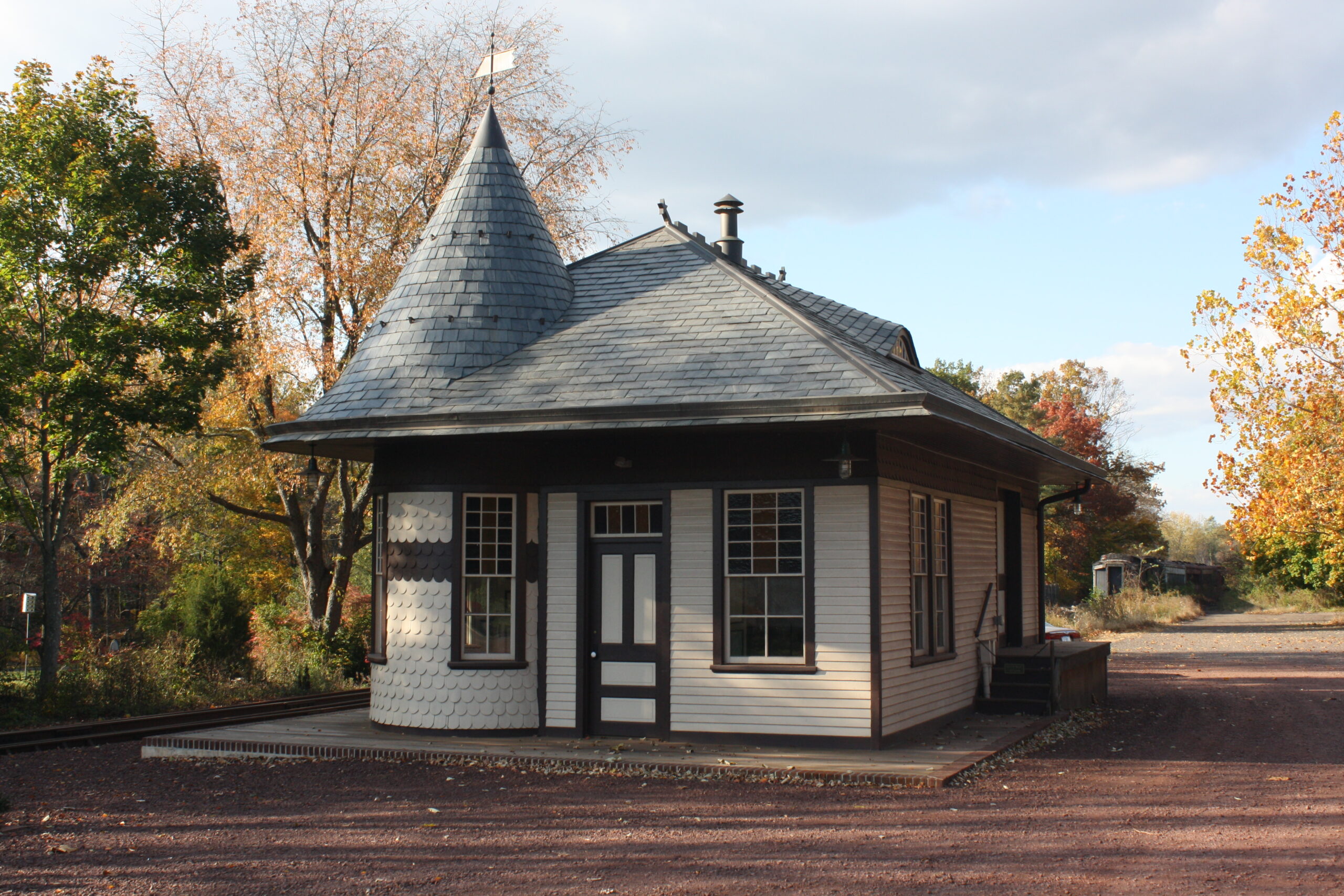 A small historic train station building in Wycombe, Pennsylvania, featuring a simple wooden structure with a sloped roof set beside railroad tracks. The station sits within the Wycombe Village Historic District, surrounded by trees and open space, reflecting the area’s late 19th-century railroad heritage.