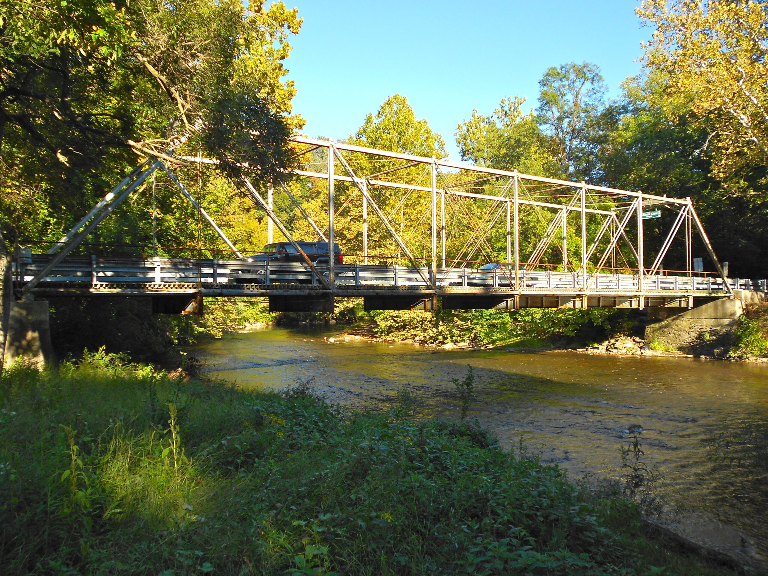 Green Lane Bridge extending across Yellow Breeches Creek with wooded banks and open sky in the background.