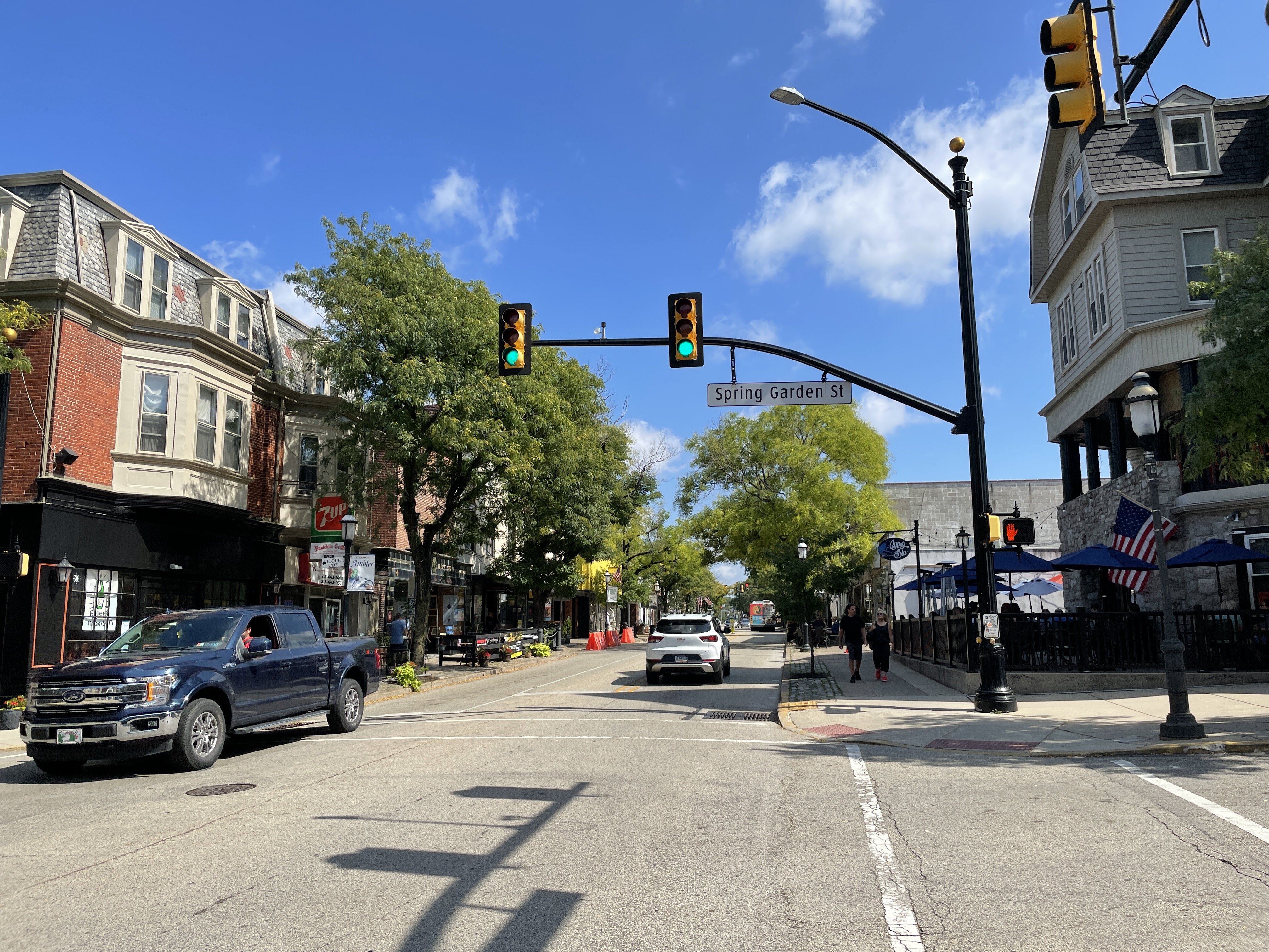 View of Butler Avenue in Ambler, Pennsylvania, showing a small-town commercial corridor with storefronts, parked cars, and roadside businesses.